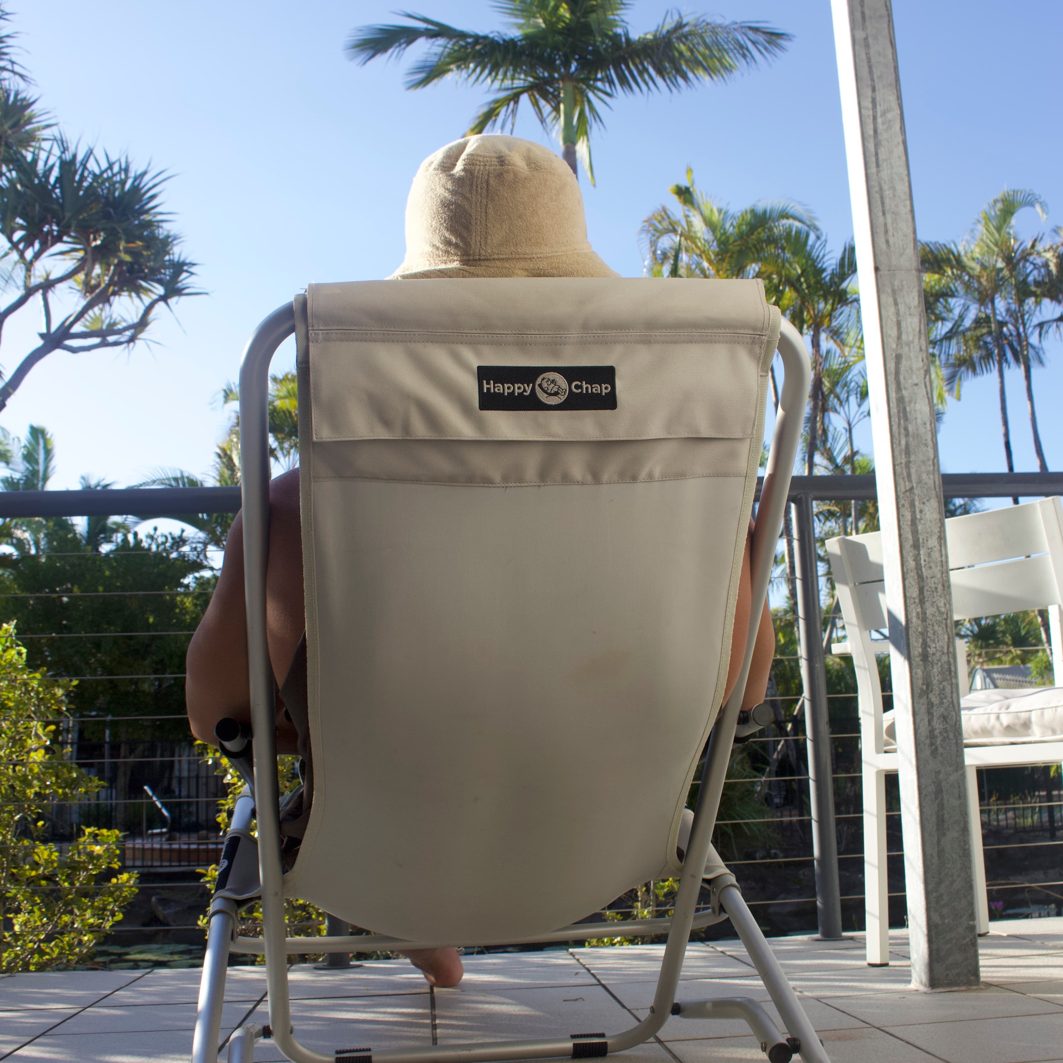 Person sitting in a beige chair with a logo on a patio with palm trees in the background