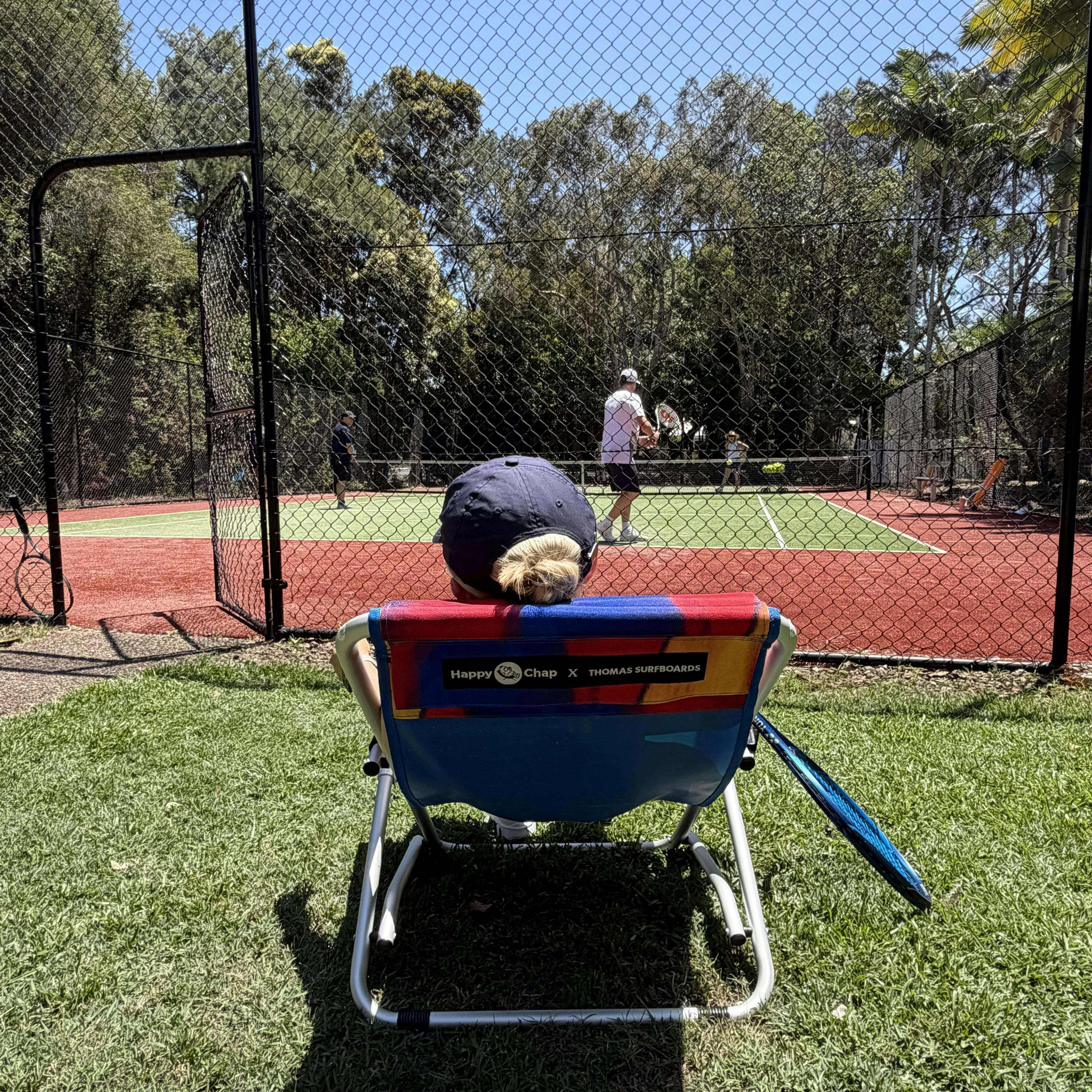 Person sitting on a colorful chair watching tennis on a court