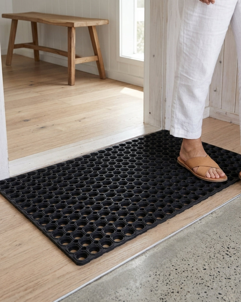 Person stepping onto a black doormat with a wooden bench in the background.