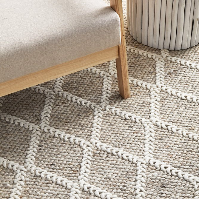 Patterned rug with geometric design on a floor next to a chair and plant.