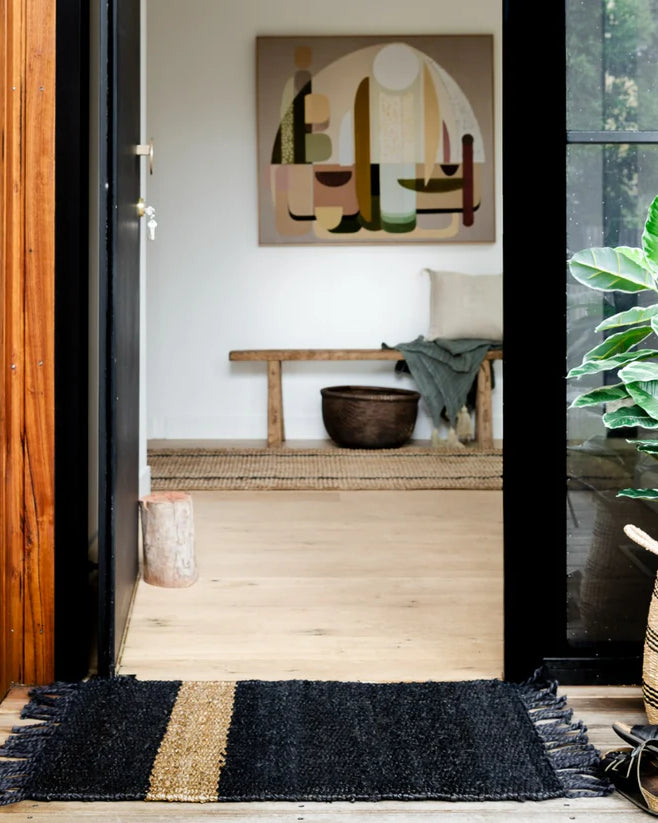 Entryway with a black and gold doormat, wooden bench, and abstract art on the wall.