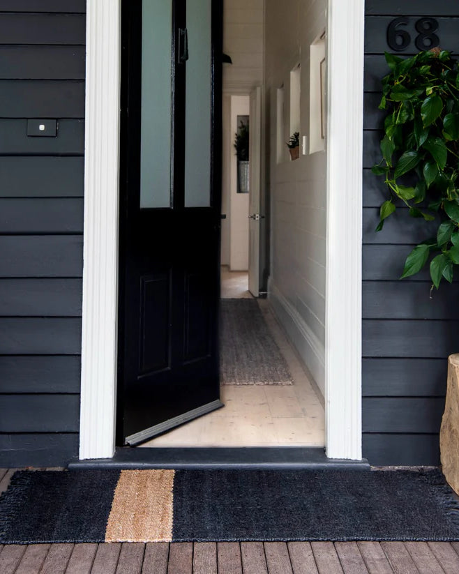 Open door leading into a house with a dark welcome mat on the wooden floor.