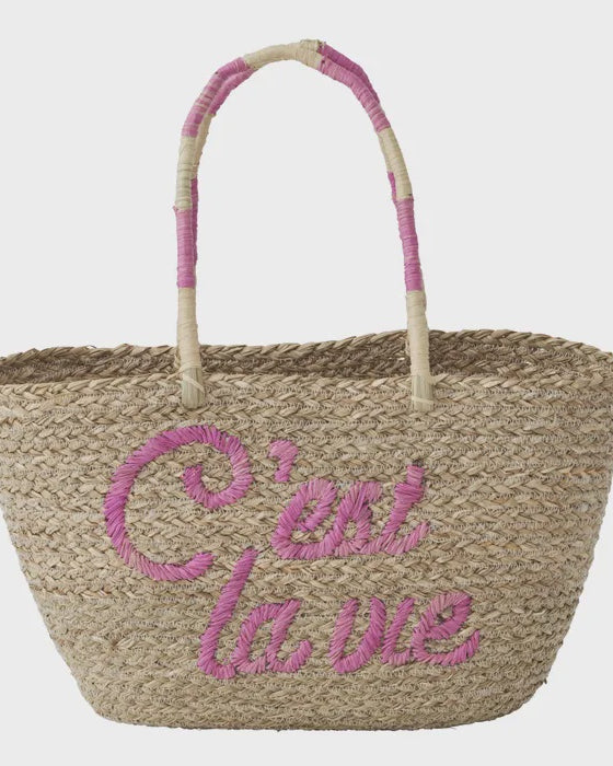 Woven basket with pink handle and 'C'est la vie' text on a light gray background