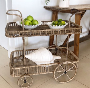 Wicker cart with two bowls of limes and a white towel on a tiled floor.