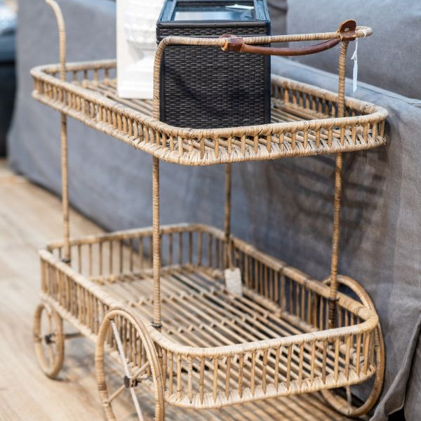 Wicker bar cart with a black lantern and white box on a wooden floor.