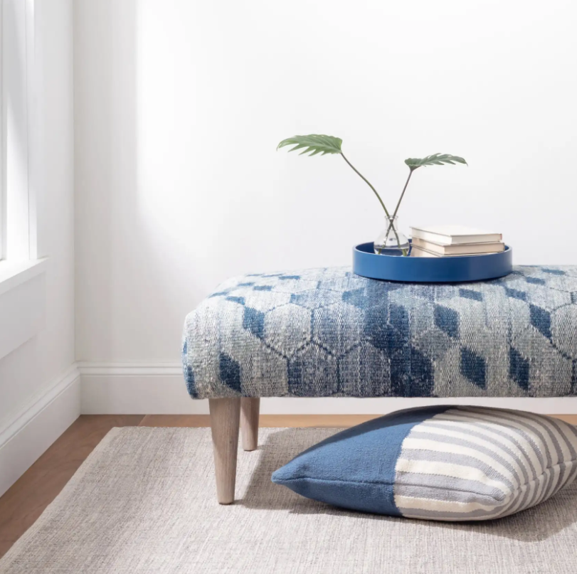 Patterned ottoman with a blue and white pillow on a light wooden floor.