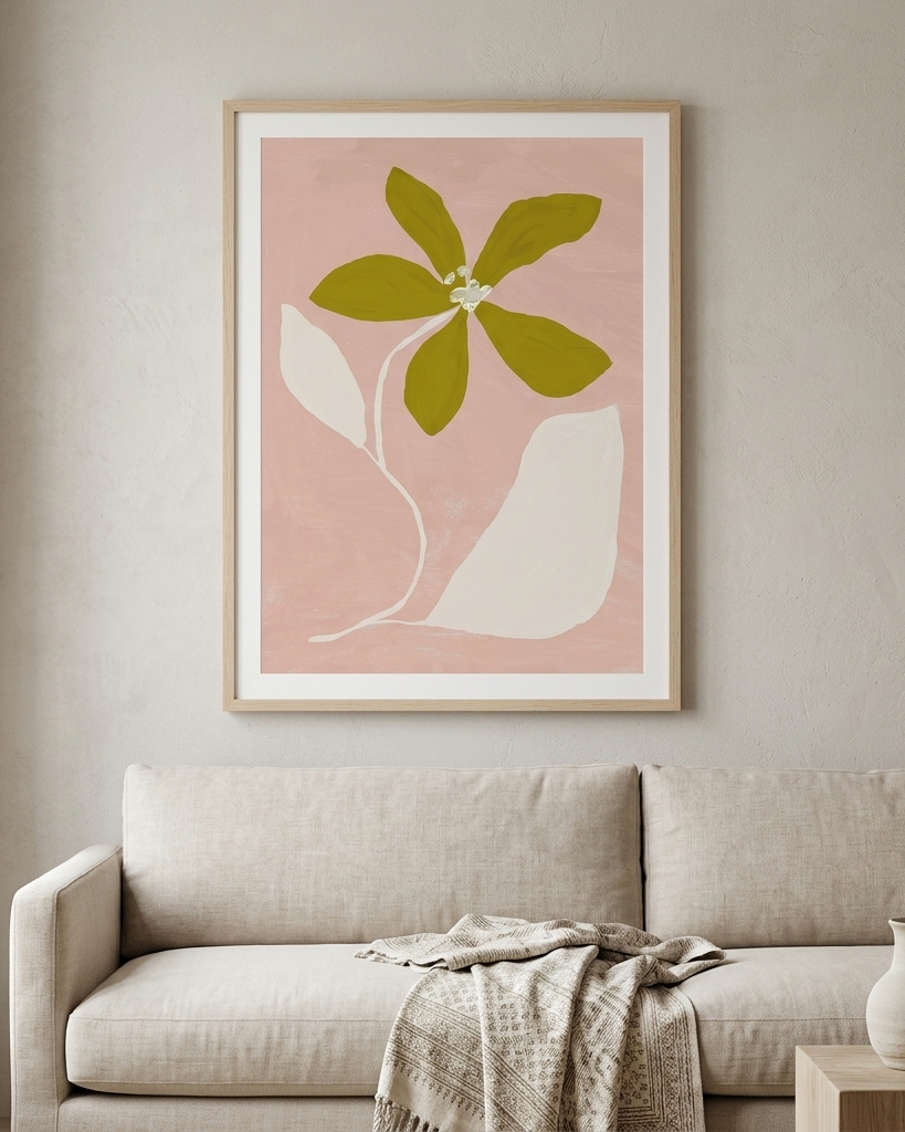 Framed botanical wall art hanging above a light beige sofa in a softly styled living room. The print features an abstract olive green flower and white leaf shapes on a dusty pink background, set in a light wood frame.