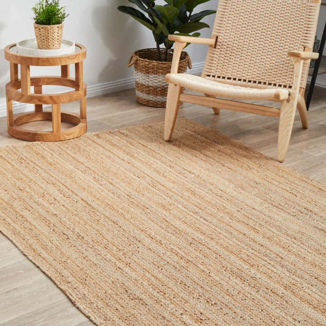 Beige jute rug on a wooden floor with a wicker chair and side table.