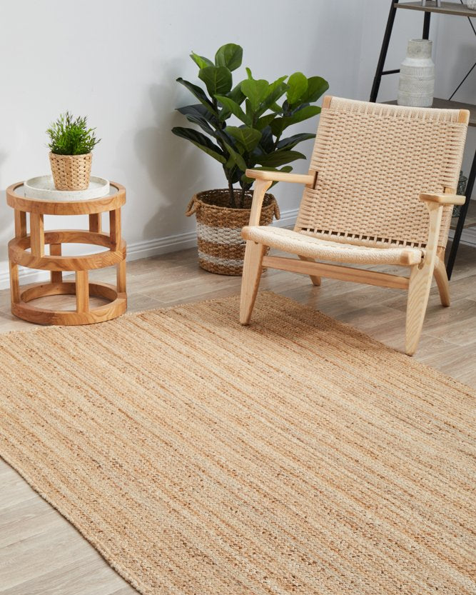 Beige jute rug on a wooden floor with a wicker chair and side table.