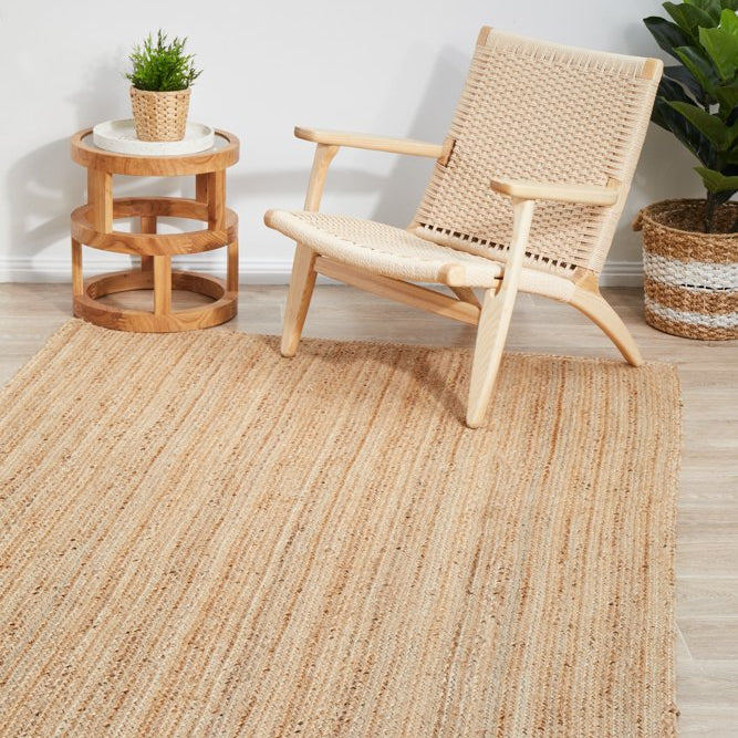 Woven chair and side table on a textured rug with plants in a minimalistic room.