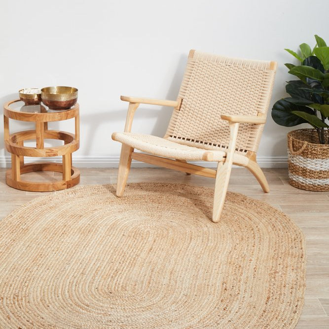 Round jute rug in a room with a wicker chair, small table, and plant.