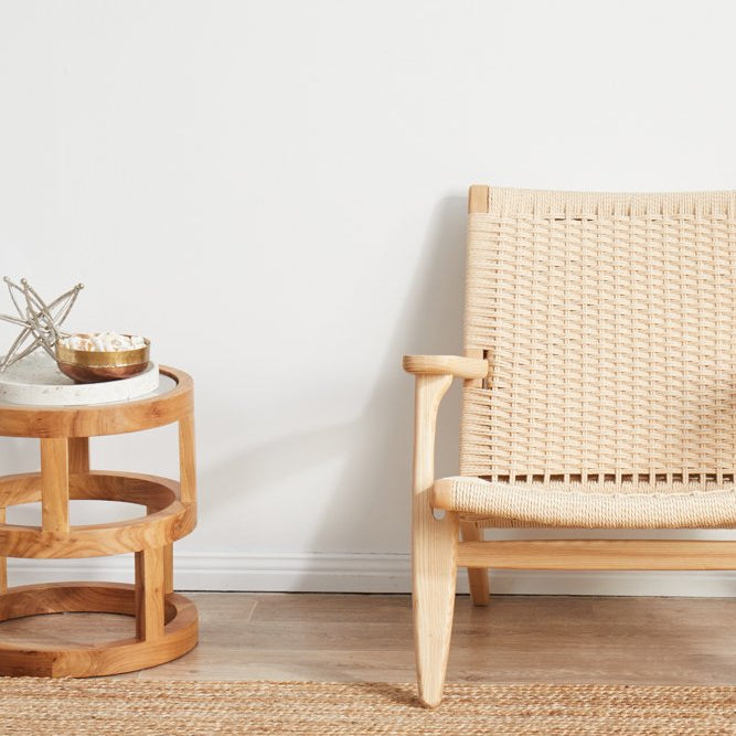 Woven chair and side table on a wooden floor with a plain white wall background