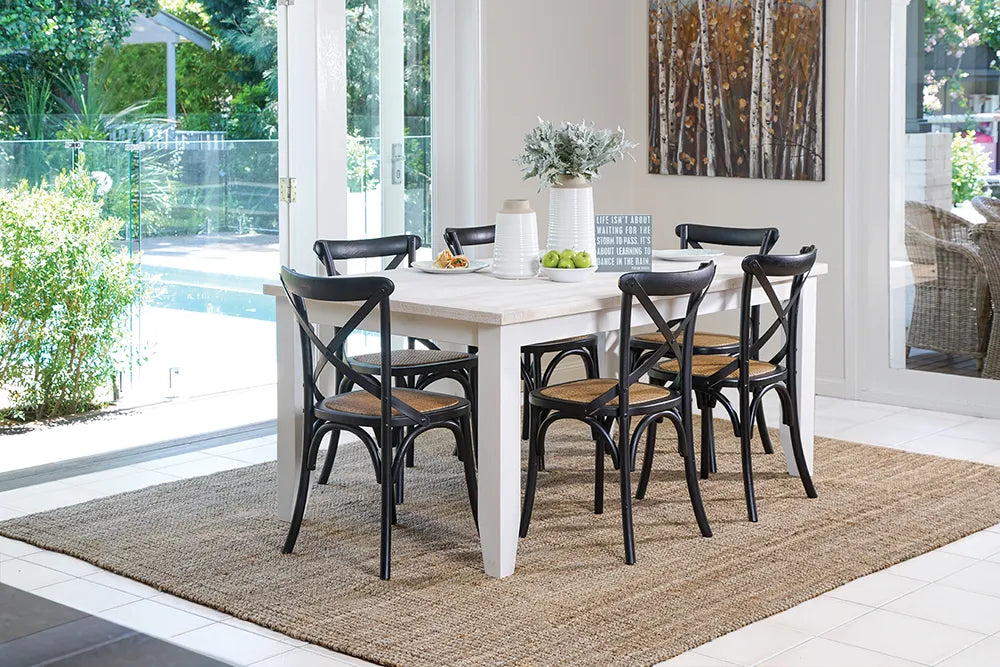 Dining area with a white table and black chairs on a jute rug, poolside.