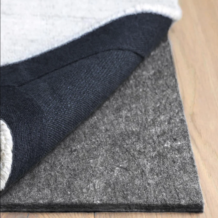 A close-up of a dark gray felt floor mat with a black backing and a light gray top layer, shown partially peeled back on a light wood floor.