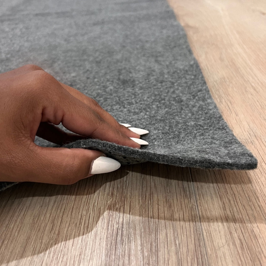 Person's hand holding a gray rug edge on a wooden floor