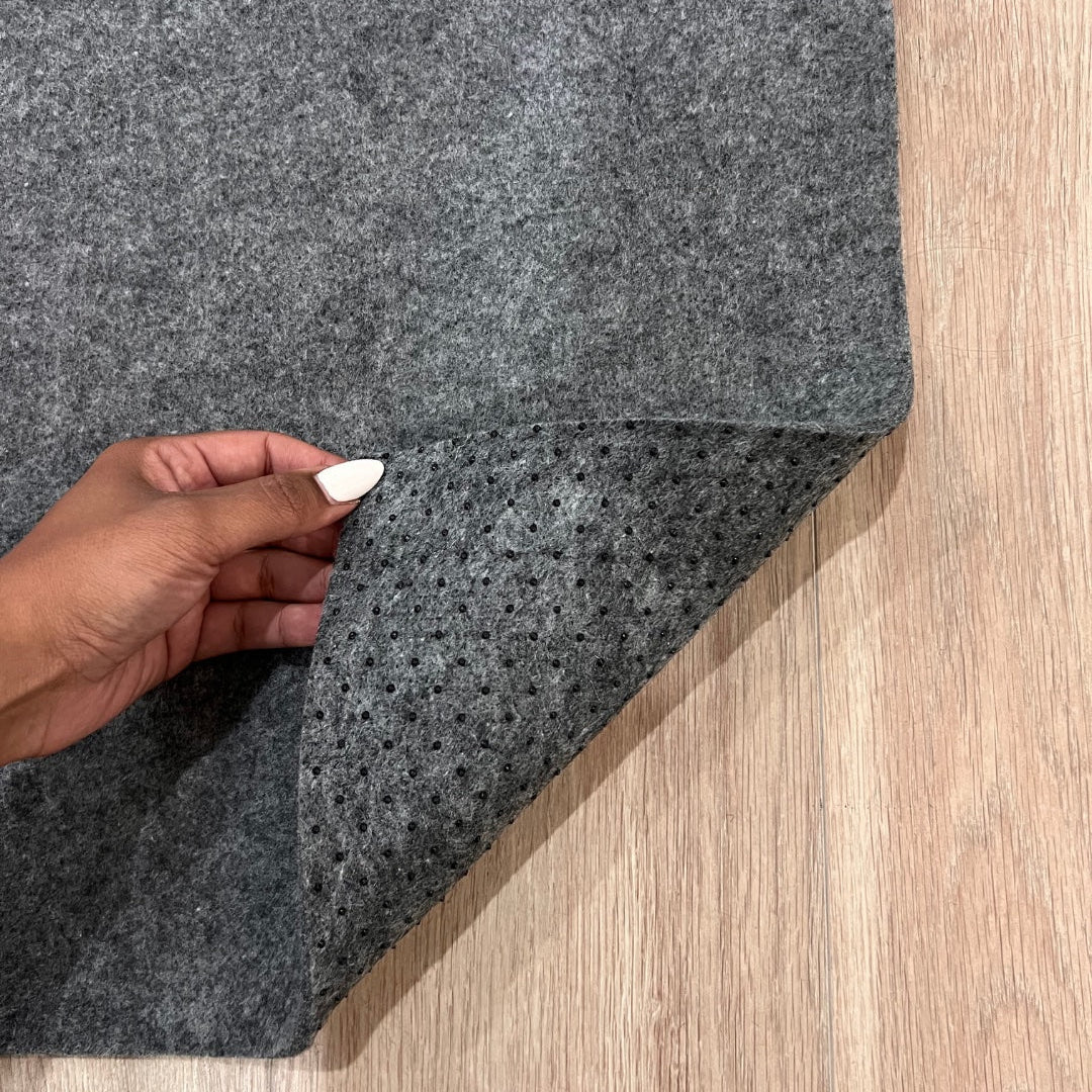 Gray carpet sample held by a hand on a wooden floor