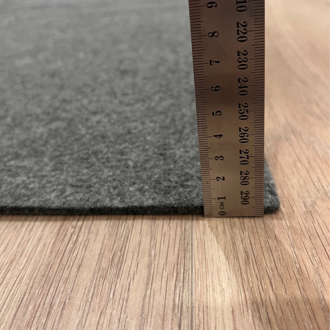 Gray carpet sample with a ruler for size reference on a wooden floor.