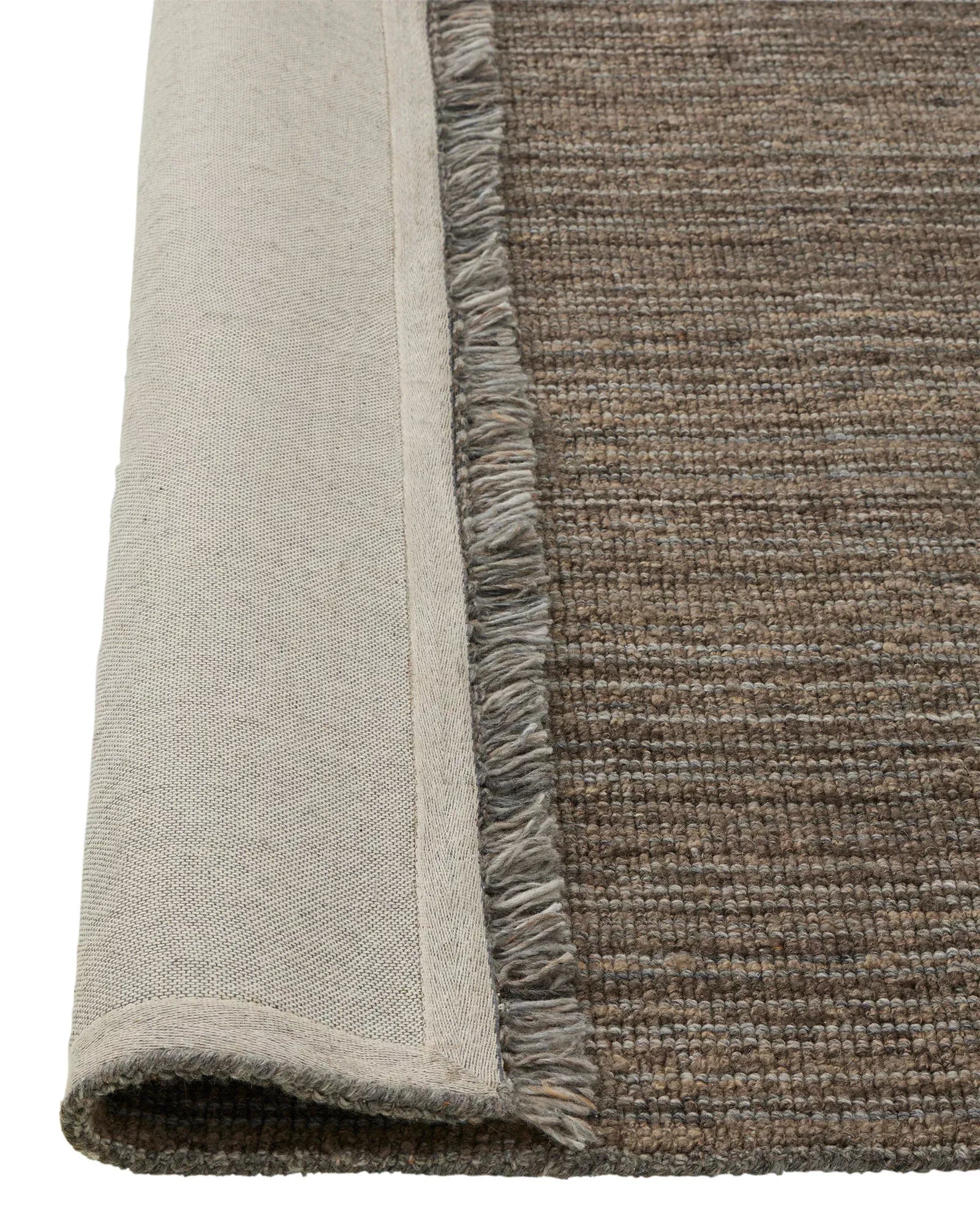 Close-up of a textured rug corner with a neutral color palette.