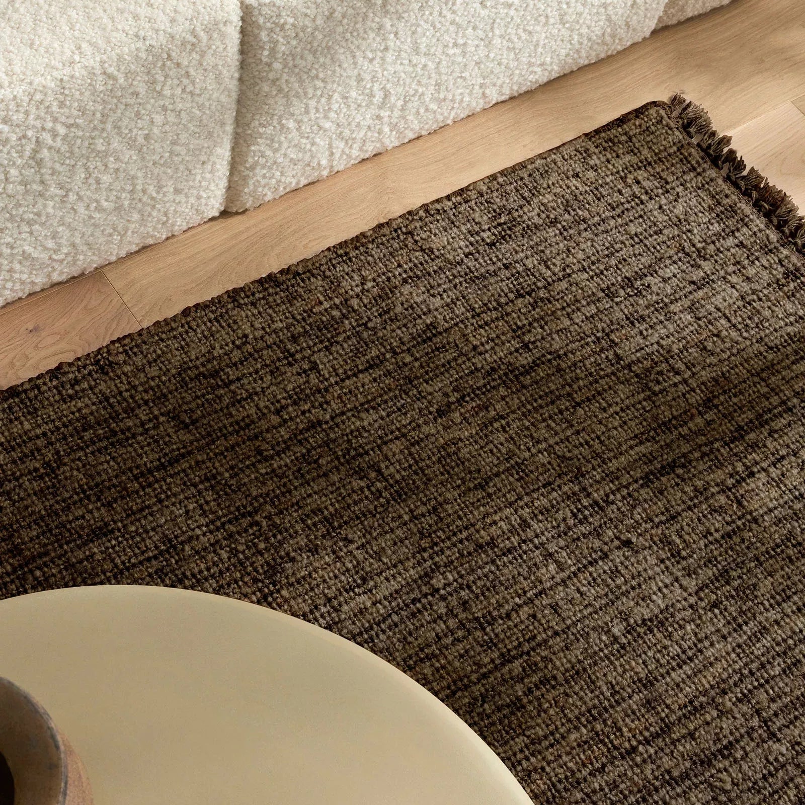 Textured brown rug on a wooden floor with a beige wall and table.