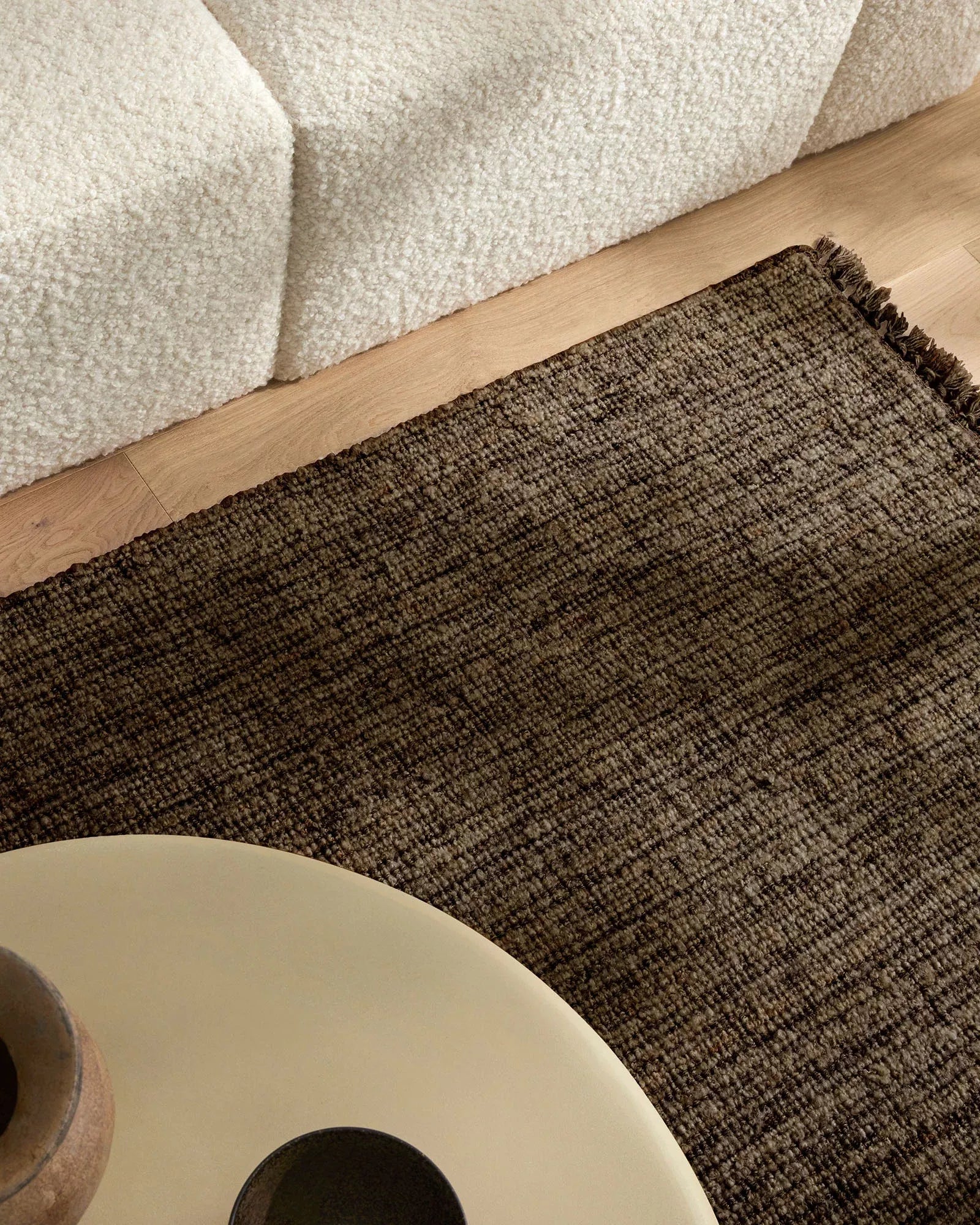 Textured brown rug on a wooden floor with a beige wall and table.
