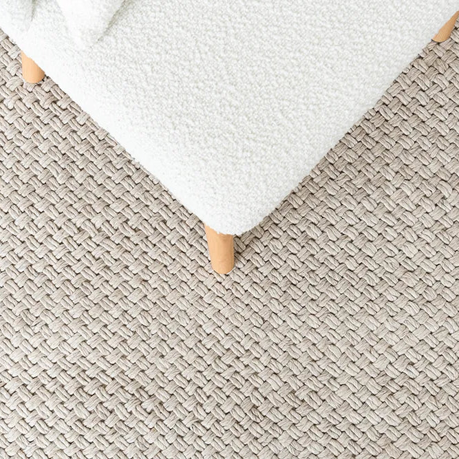 Close-up of a textured beige carpet with a white ottoman corner.