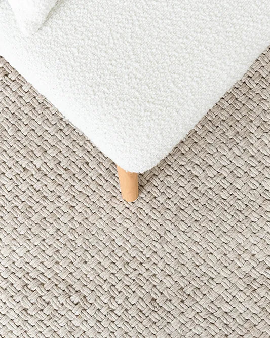 Close-up of a textured beige carpet with a white ottoman corner.