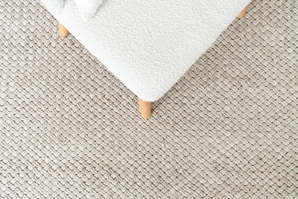 Close-up of a textured beige carpet with a white ottoman corner.