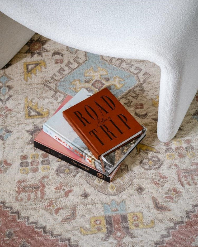 Stack of books on a patterned rug with a white chair partially visible