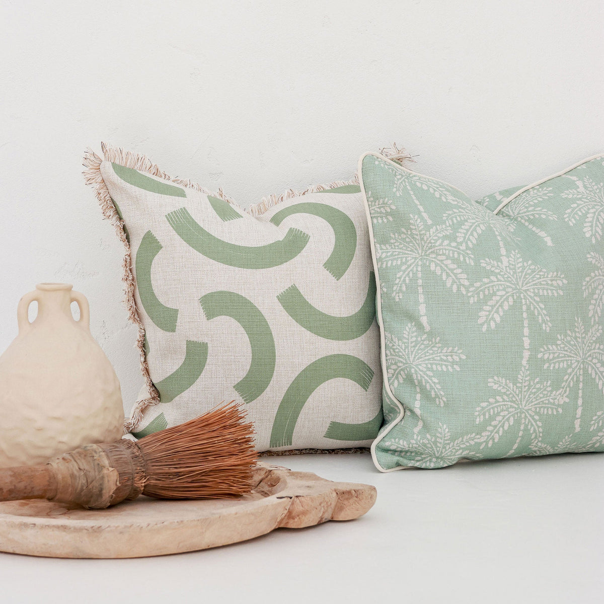 Two patterned pillows on a white surface with a vase and brush.