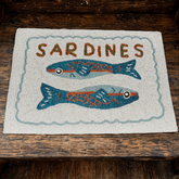 Textile with 'Sardines' and fish illustrations on a wooden surface