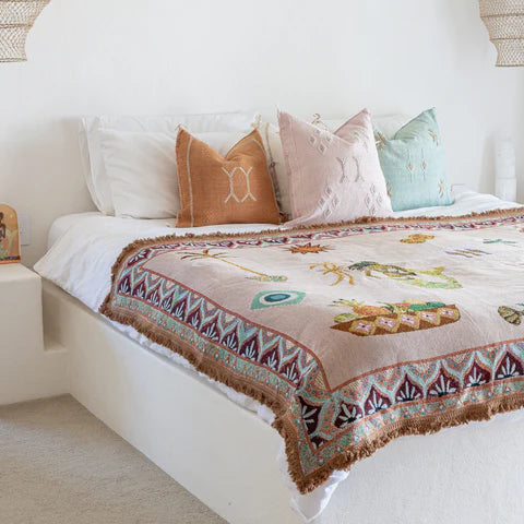 Bedroom with a bed featuring a patterned throw and pillows, next to a wicker chair.