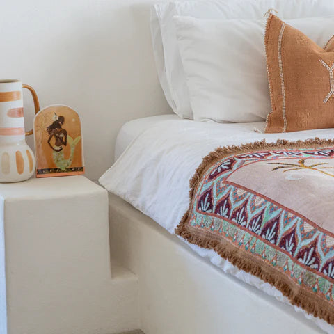 Bedroom with a bed featuring patterned throw and pillows, a nightstand with decorative items, and a chair.