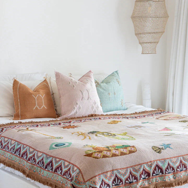 Bed with patterned quilt, colorful pillows, and a hanging lamp in a bedroom setting.