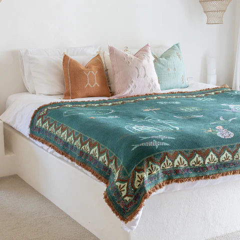 Bed with a green patterned throw and colorful pillows in a bedroom setting.