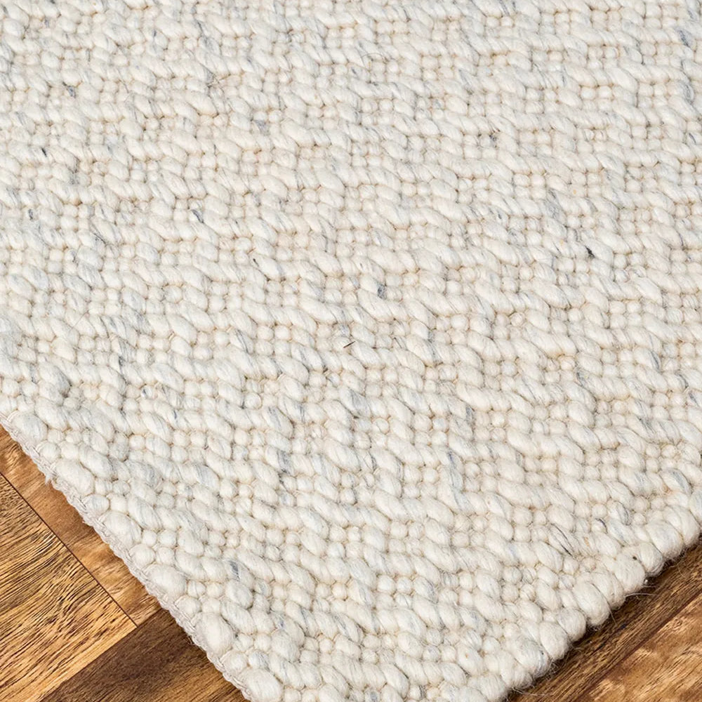 Close-up of a textured white rug on a wooden floor