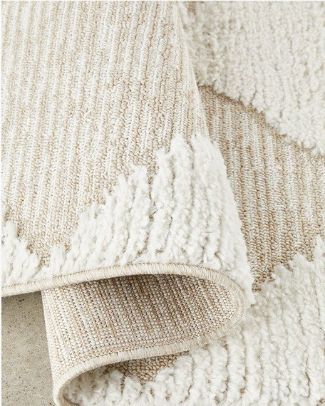 Close-up of a textured beige and white rug on a concrete floor.