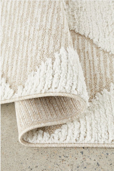 Close-up of a textured beige and white rug on a concrete floor.