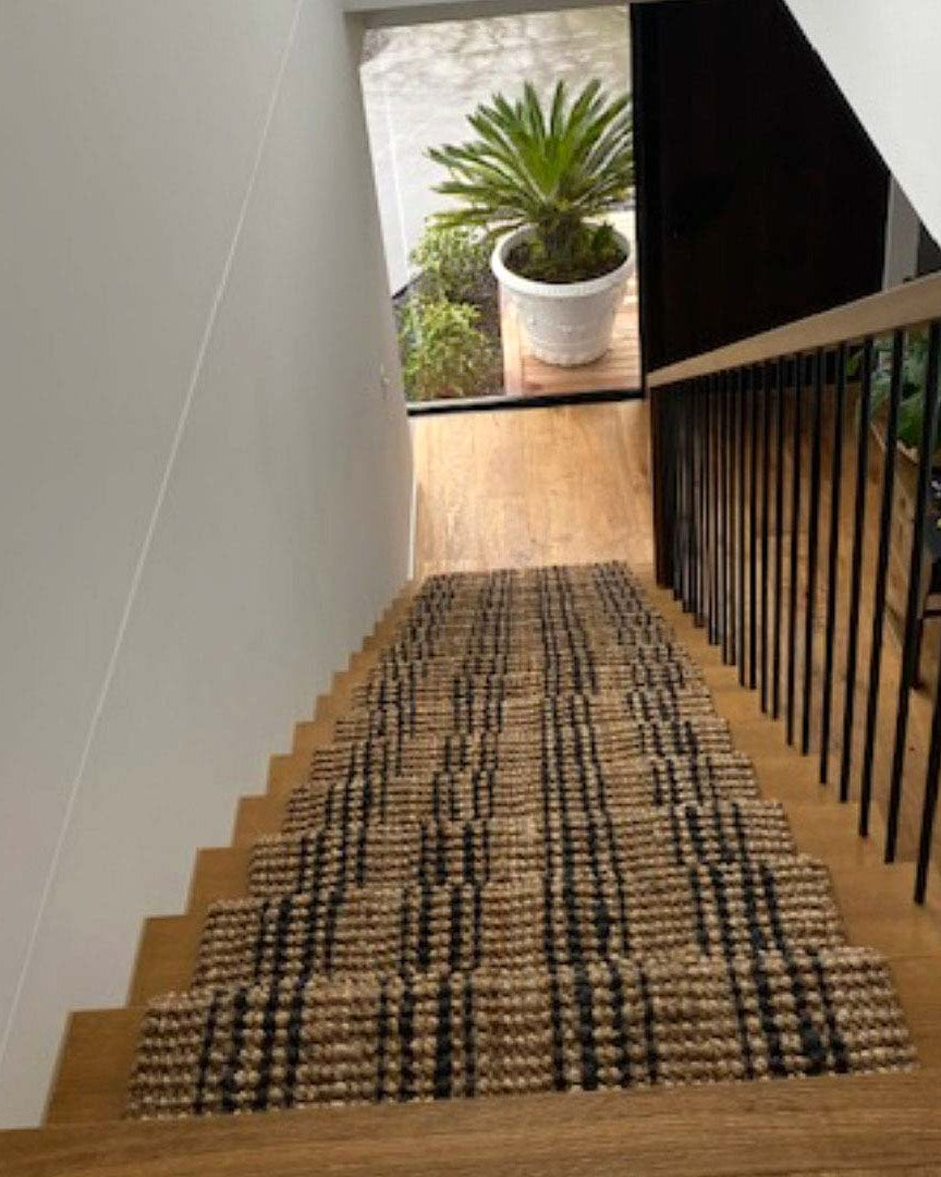 Staircase with a textured runner leading to an outdoor area with plants.