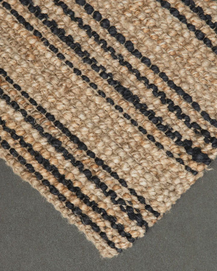 Close-up of a woven jute rug with black lines on a gray background