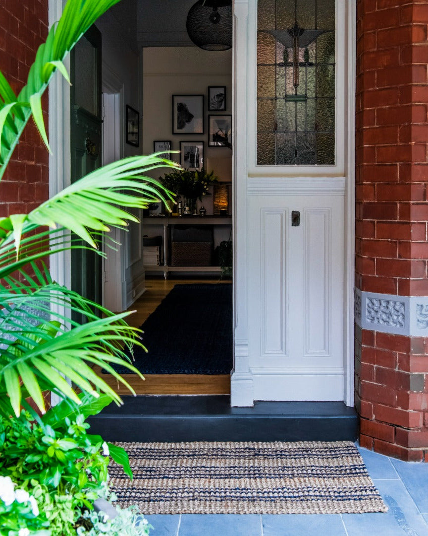 Front door of a house with a doormat, plants, and a view into the interior.