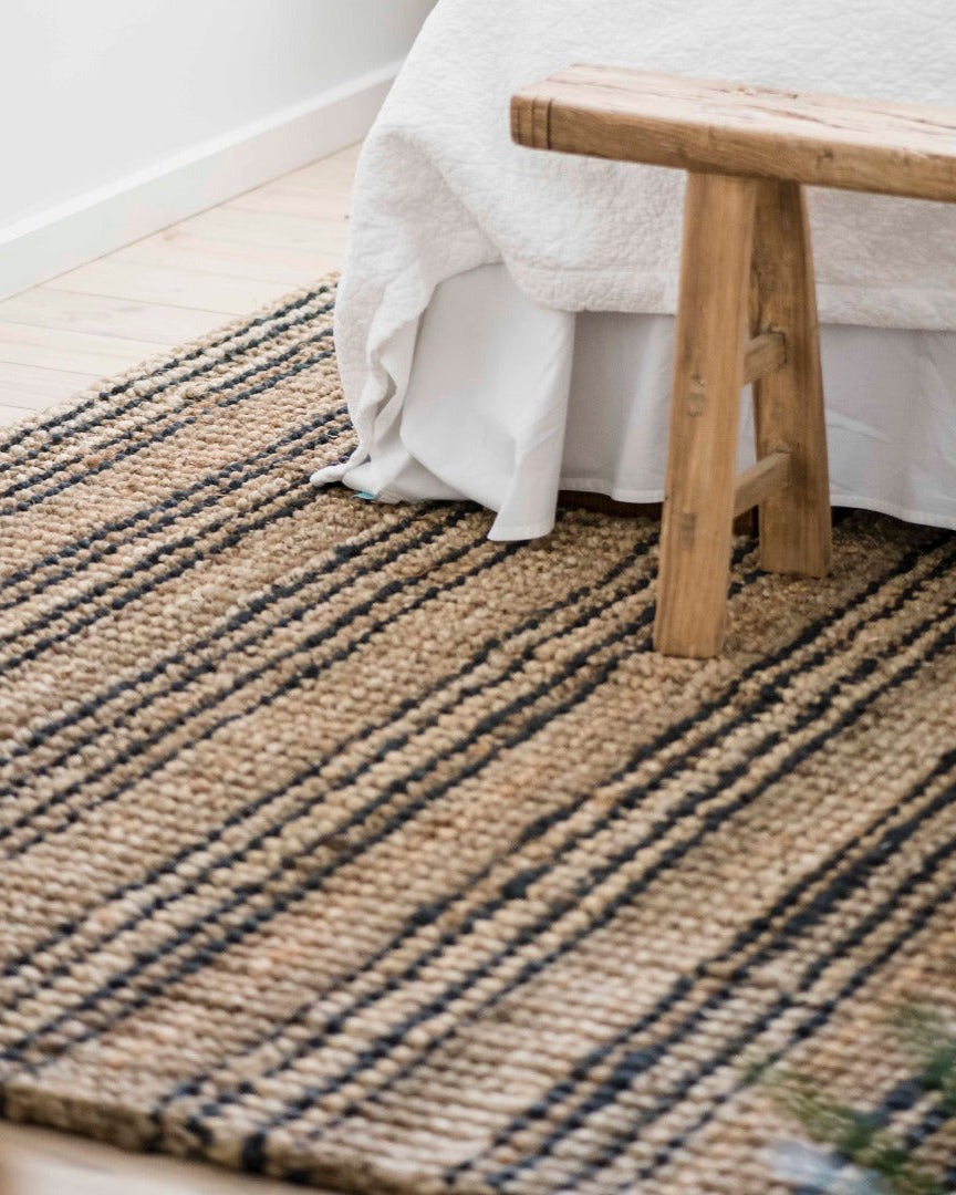 Woven jute rug with a wooden bench and white fabric in a room setting.