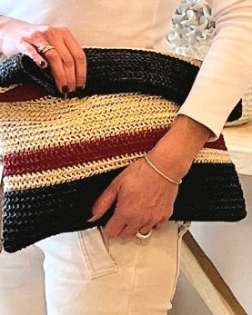 Person holding a striped woven clutch bag with black, red, and beige colors.