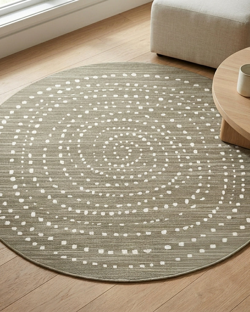 A round area rug with a textured taupe-gray base and a white dotted spiral pattern, styled on a light wood floor next to a wooden coffee table and a light beige ottoman.