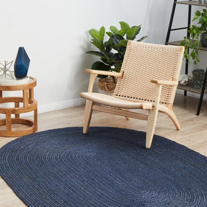 Round blue rug on a wooden floor with a wicker chair and plants in the background.