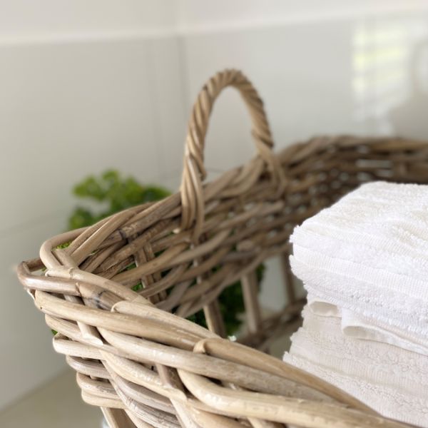 Wicker basket with white towels and greenery on a neutral background