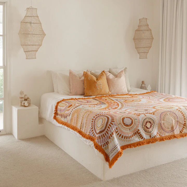 Bedroom with a bed covered in a patterned orange and white blanket, surrounded by neutral decor.