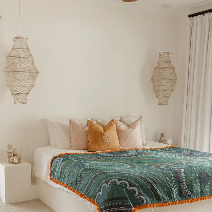 Bedroom with a bed featuring a green and orange patterned blanket, surrounded by decorative lamps and a ceiling fan.