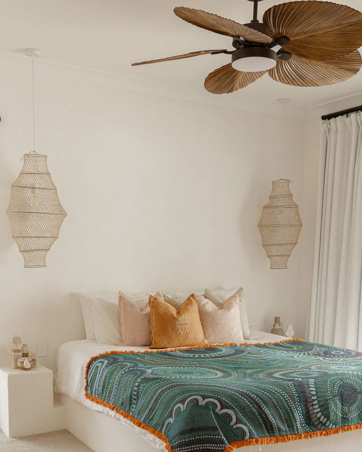 Bedroom with a bed featuring a green and orange patterned blanket, surrounded by decorative lamps and a ceiling fan.