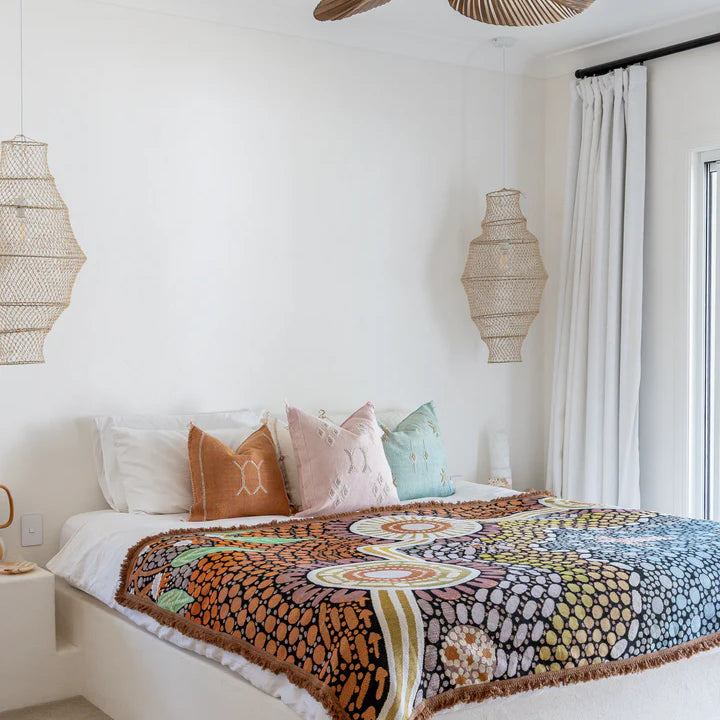 Bedroom with a colorful patterned blanket on a bed, wooden ceiling fan, and decorative lamps.