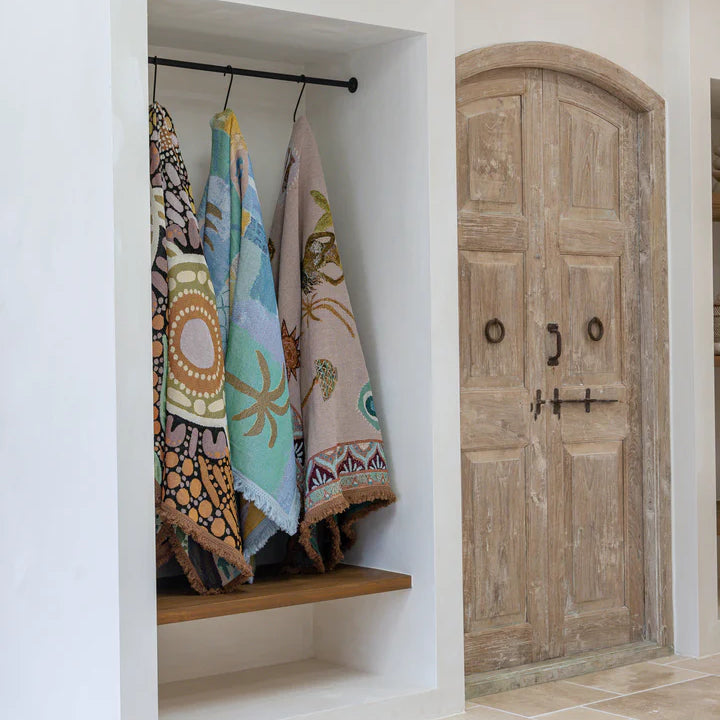Closet with throw rugs hanging on a rack and a wooden door in the background.